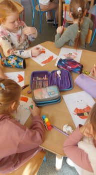 Zdjęcie przedstawia dzieci siedzące przy stoliku i koloryzujące obrazek św. Mikołaja.