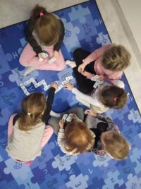 Na zdjęciu dziewczynki siedzące na dywanie i układające puzzle.