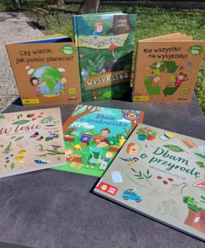 Zdjęcie przedstawia stolik w parku, a na nim rozłożone książki o tematyce ekologicznej dla dzieci.