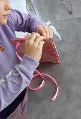 Zdjęcie przedstawia dziecko przy stoliku trzymajęce w rękach notatnik obłożony materiałem.
