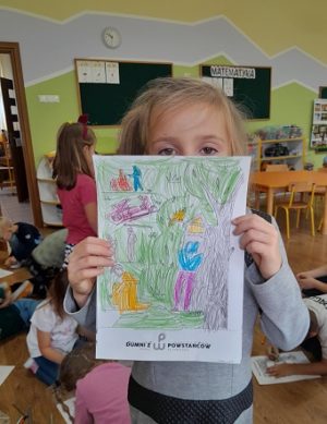 Na zdjęciu widoczne dziecko trzymające przed sobą kartkę z rysunkiem.