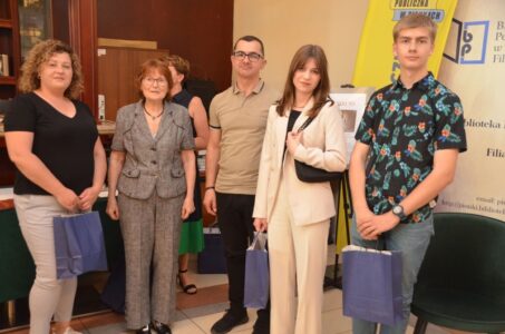 Na zdjęciu widać stojących ludzi w sali, w tle banery instytucji.
