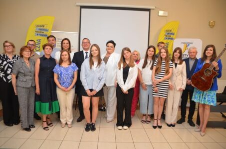 Zdjęcie przedstawia ludzi ustawionych do zdjęcia grupowego w sali. Z tyłu widać banery instytucji i ekran.