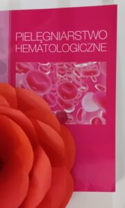 Zdjęcie okładki książki Pielęgniarstwo hematologiczne z położonym na niej czerwonym kwiatem z papieru.
