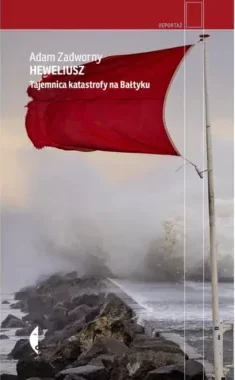 Zdjęcie okładki książki Adama Zadwornego "Heweliusz". Na pierwszym planie widoczny skalisty brzeg morza. Po prawej stronie czerwona flaga na białym maszcie. Nazwisko autora i tytuł u góry.