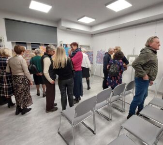 Na zdjęciu widać ludzi w sali oglądających obrazy.