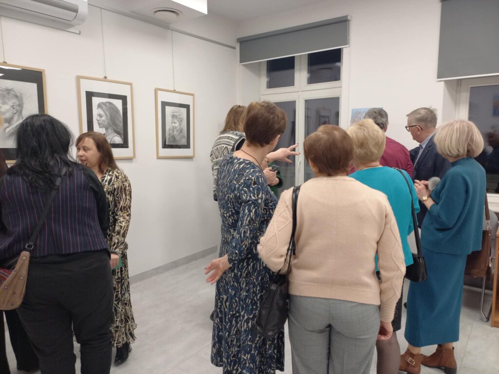 Na zdjęciu widoczny fragment sali wraz ze zgromadzonymi ludźmi, oglądającymi obrazy wiszące na ścianie.