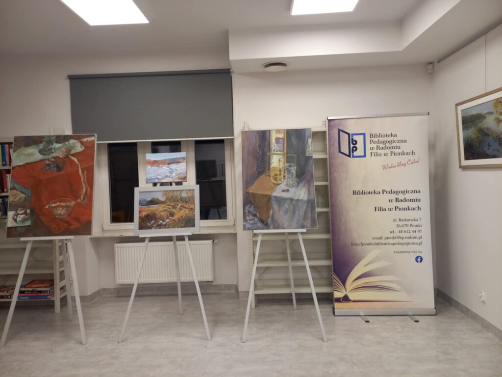 Na zdjęciu widoczne obrazy na sztalugach, obok duży baner instytucji, Wszystko w sali.