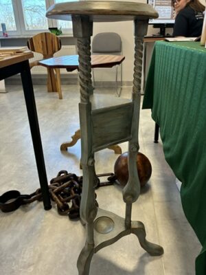 Na zdjęciu widoczne różne przedmioty wykonane z drewna: 2 różne stoliki, kula z łańcuchem, krzesło.