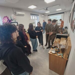 Na zdjęciu widoczna młodzież. Dwaj chłopcy w mundurach leśników, obok nich eksponaty związane z zawodem, pozostałe osoby oglądają, słuchają.