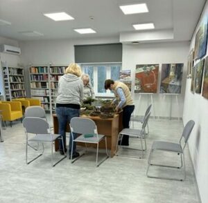 Na zdjęciu kobiety skupione wokół stolika w sali, przed nimi widać zielone gałązki.