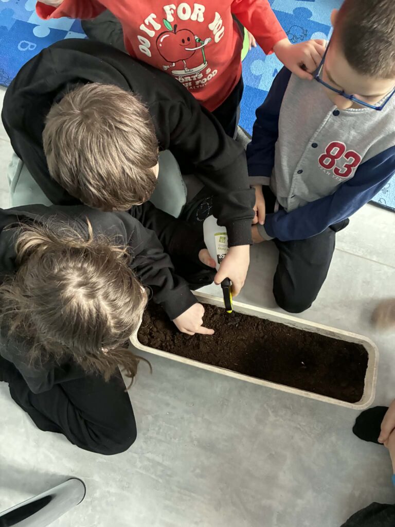 Na zdjęciu dzieci pochylone nad skrzynką z ziemią.