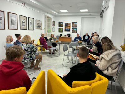 Na zdjęciu widać salę wystawową, ludzi siedzących przy stolikach.